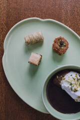 drinking chocolate in matching green cup and plate with assorted baklava desserts on wood table