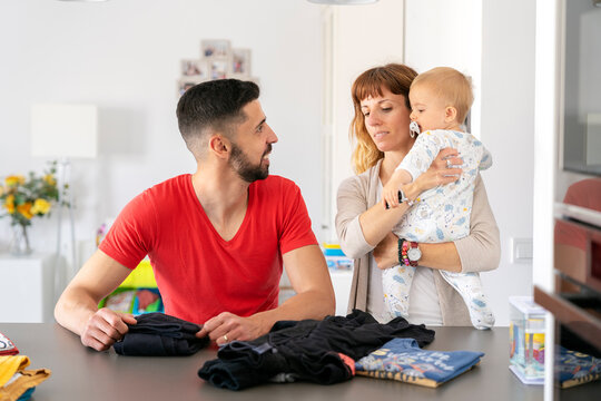 husband and wife talking, son in arms, tidying laundry
