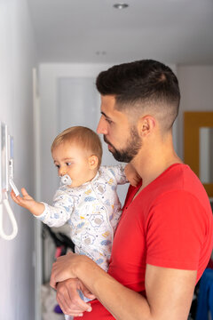 Father With His Son In His Arms Looking At Thermostat