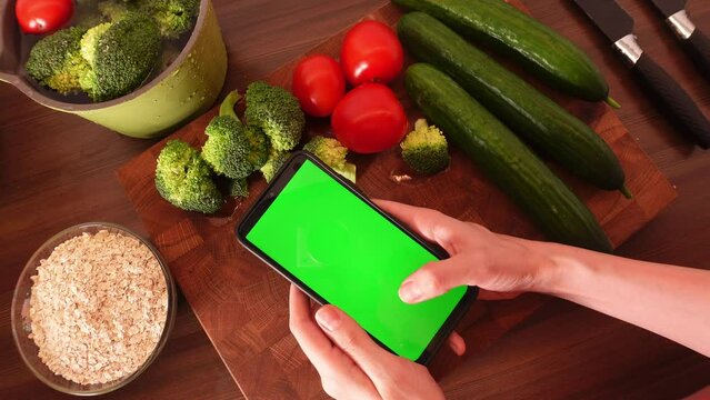 Young woman orders food online using a smartphone.Woman using black smartphone with green screen.Hands of person scrolling up photos,scrolling catalogs, pressing finger, reading social media internet