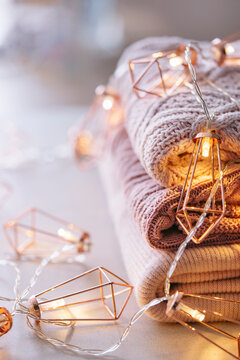 Stack of knitted sweaters with fairy lights garland.
