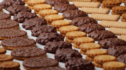 Close-up photo of beautiful chocolate glazed cookies, round filled and rectangular crackers stacked in rows in a beautiful pattern