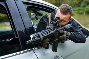 One man special force police or terrorist holding automatic weapon shooting and aiming from the car...