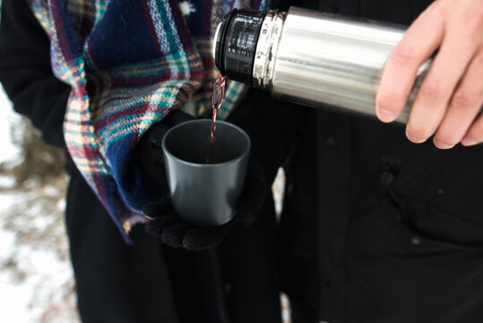 Anonymous person pouring tea from thermos in the winter