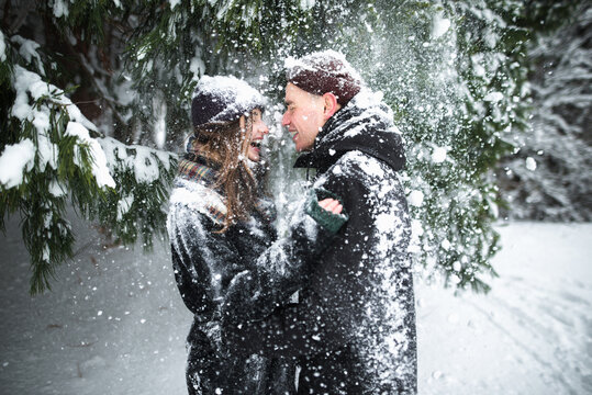 Young couple laughing covered with snow under the trees