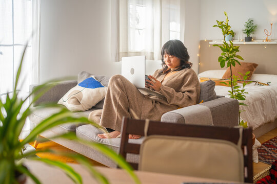 Asian Girl Working From Home With Laptop On The Couch.
