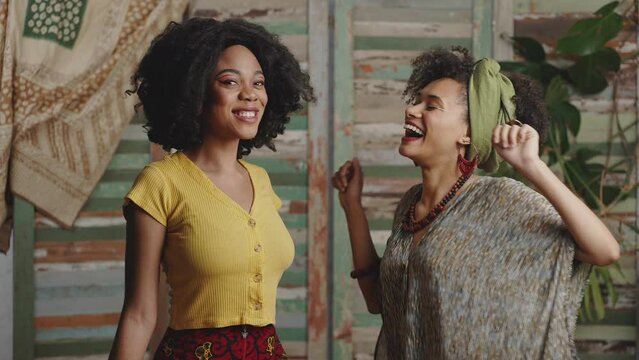 Two stylish african american ladies dancing together, enjoying dynamic music at rustic interior, slow motion