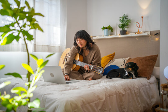 Girl In Pyjama Playing The Guitar On The Bed With Dog