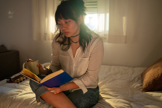 Asian Girl Reading A Book On The Bed At Home