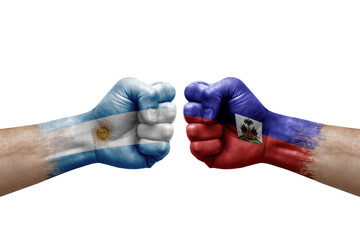 Two hands punch to each others on white background. Country flags painted fists, conflict crisis concept between argentina and haiti