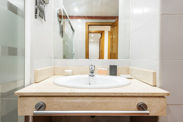 front view of white earthenware sink on top of cream-colored marble with veining, mirror embedded in the wall and glass partition
