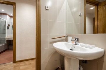 WC with white porcelain sink with built-in mirror, cream tiles and another WC across the hall