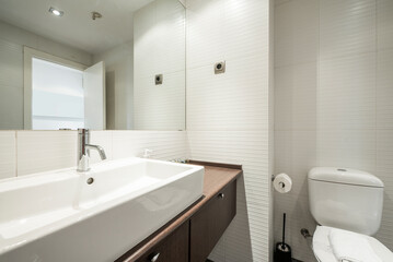 Fototapeta na wymiar Bathroom with dark wood cabinets with drawers and white porcelain sink, rectangular frameless mirror