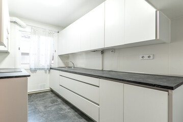 Furnished kitchen with elongated black countertop and plain white cabinets