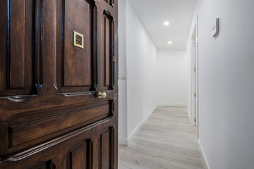 Vintage wooden entrance door to a residential apartment home with gray wooden floorboards and white painted walls