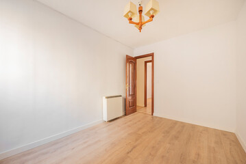 empty room with light wood floors, mahogany woodwork on the doors, electric storage radiator and wooden ceiling light
