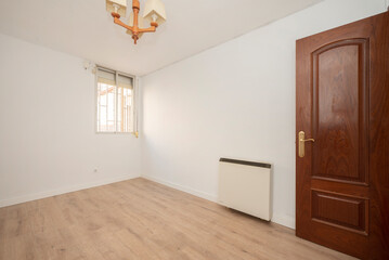 empty room with light wood floors, mahogany woodwork on the doors, electric storage radiator and aluminum window in the background