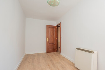 empty room with light wood floors, mahogany woodwork on the doors, electric storage radiator