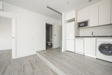 Living room and kitchen of apartment on two levels with white kitchen furniture and ceramic tile floors