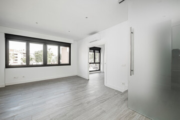 Empty living room in a loft with large black aluminum windows with gray wood-like ceramic floors...