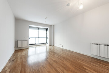 Empty living room with white aluminum radiators and long slat oak parquet flooring with black aluminum window and translucent white blinds