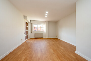 living room empty of furniture with wooden floors, freshly painted walls and access to a glazed terrace