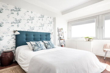 bedroom with a king size bed with a blue upholstered headboard and wallpapered walls with plants...