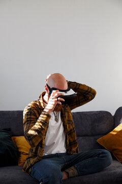 Man putting on VR goggles on sofa