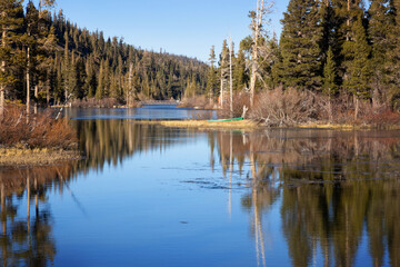 Green Canoe onshore at Twin Lakes in winter at Mammoth Lakes, California. Calm lake water with...