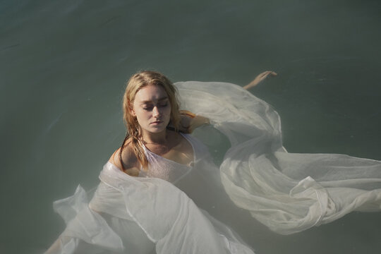 Blonde Woman In White Dress Floating On Water 