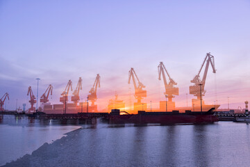 Fototapeta premium In the setting sun, the crane at the coastal wharf is lifting goods for the cargo ship, with double photographic effects.