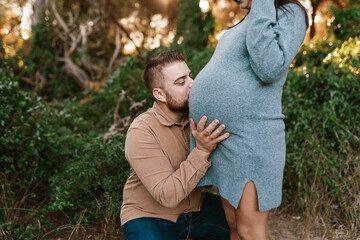Bearded future father hugging and kissing belly of wife