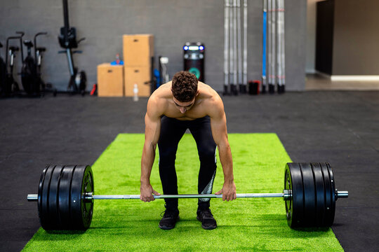 Shirtless weightlifter deadlifting barbell in gym