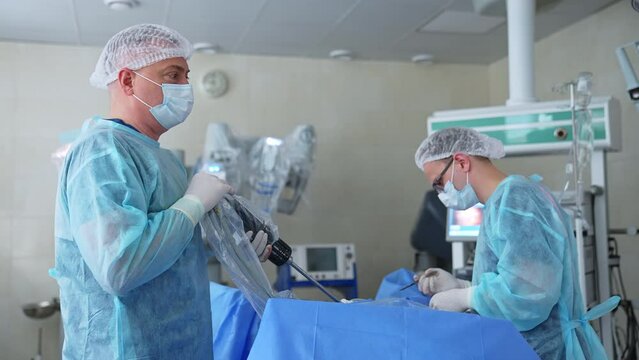 Professional surgeons conduct the operation. One surgeon holds a technological device and the other uses scalpel. Blurred backdrop.