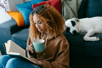 Teenage girl reading and drinking tea at home