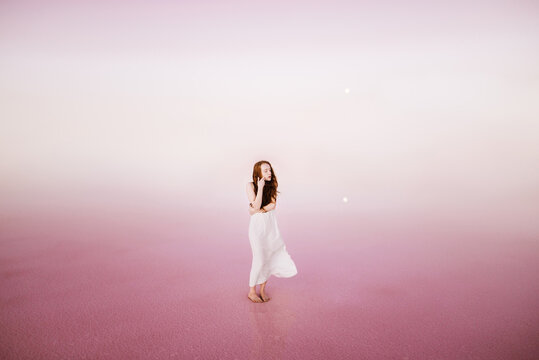Red head woman in a white dress on the pink background 