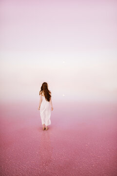 A young woman standing on the shore of a pink lagoon  