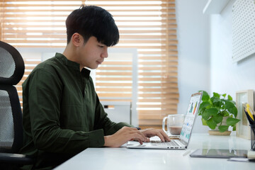 Handsome young asian man working online with laptop computer at modern home office.