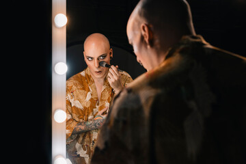 Trendy gay man applying makeup in dressing room