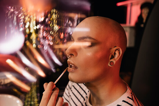 Young gay man applying makeup in dressing room
