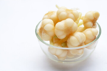 Pickled garlic in glass bowl on white background.