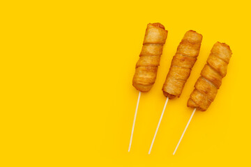 Fried dough snacks wrapped sausage on yellow background.