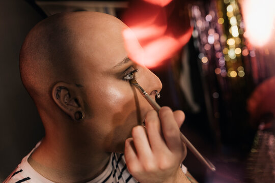 Young gay man applying makeup in dressing room