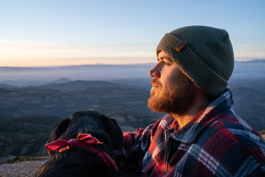Man with his dog sitting in mountain peak at sunset
