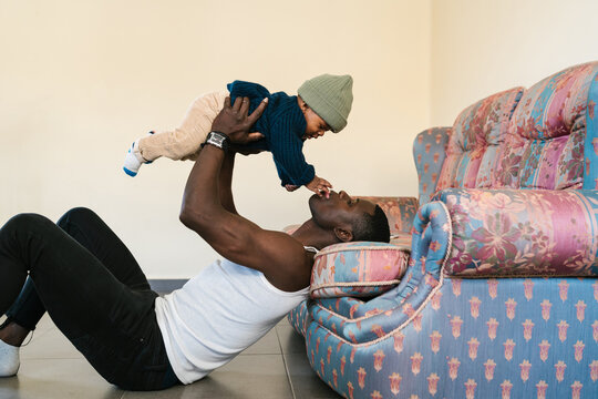 Black dad playing with toddler near settee