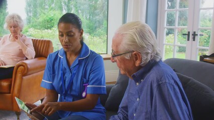 Senior couple at home with woman talking to female nurse or care worker using digital tablet - shot in slow motion