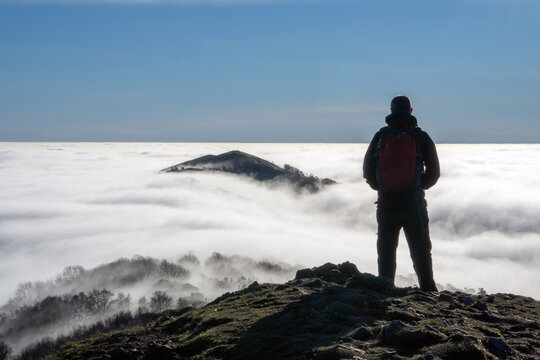 A man on top of a hill looking down on a cloud inversion 