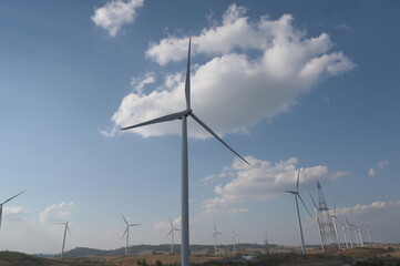 Windmills are lined up in a long row. The scattered white clouds contrasted with the blue sky. The...