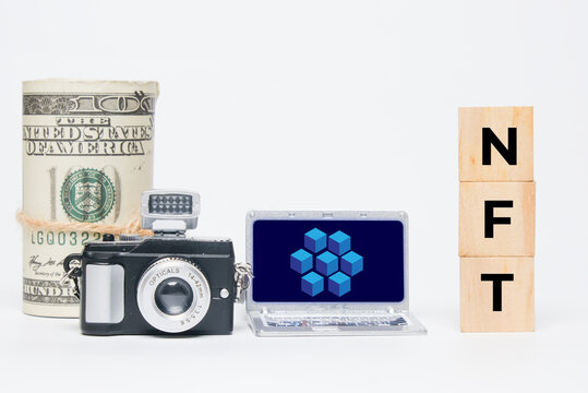 A miniature camera, laptop with blockchain, fake money and NFT word. A non-fungible token trading concept.