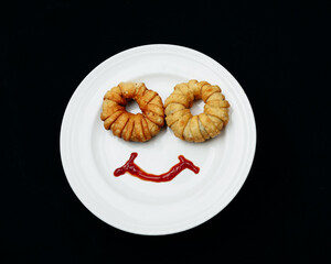 Round shape vegetable patties on a white plate with a smiley design made from ketchup
